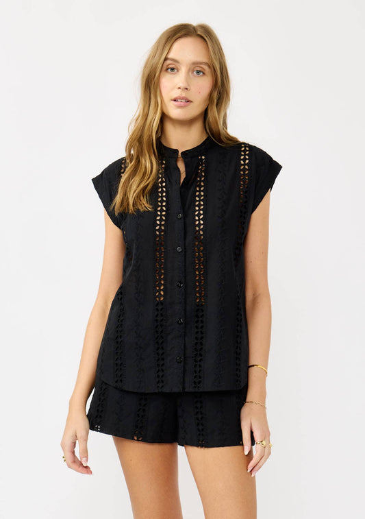 A woman wearing a black floral eyelet mandarin collar camp shirt with short sleeves and a straight bottom hem.